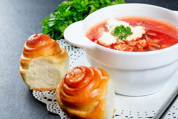 Gebäckröllchen neben einer Roten Beete Suppe mit Kräutern und saurer Sahne