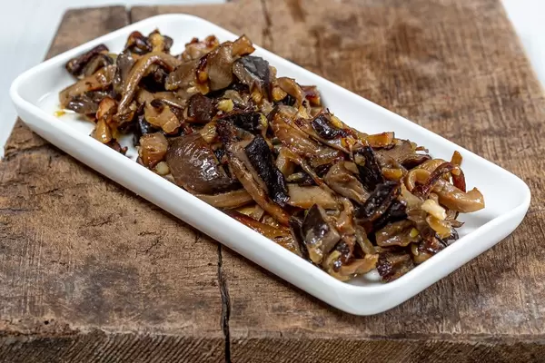 Gebratene Austernpilze mit Zwiebeln auf rustikalem Holzbrett