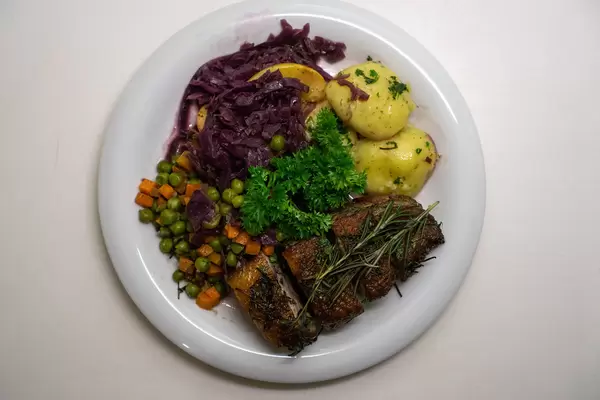 Gebratene Entenbrust mit Rosmarin, Erbsen, Karotten, Apfel-Rotkohl, Kartoffelknödel und Petersilie von oben fotografiert