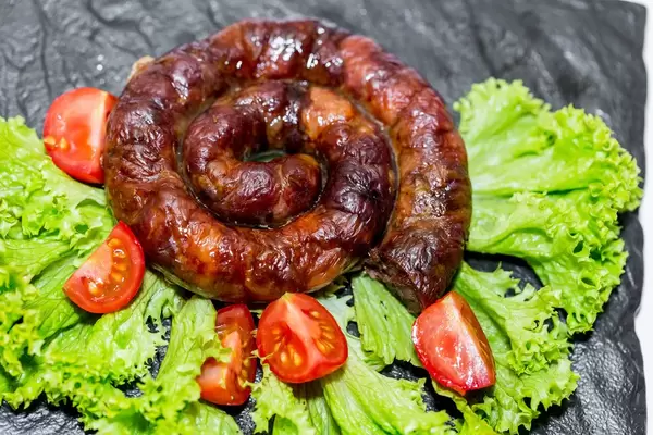 Gebratene, frische Wurstschnecke auf Salatblättern und dekoriert mit Tomaten vor schwarzem Hintergrund