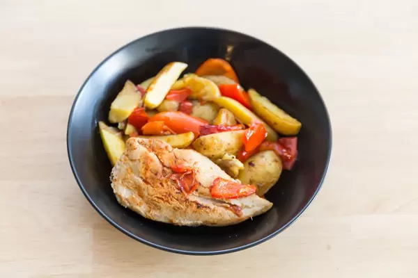 Gebratene Hähnchenbrust mit Ofenkartoffeln und Paprika auf einem schwarzen Teller