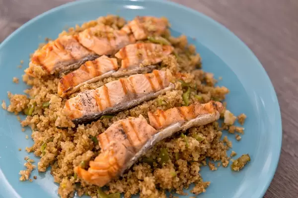 Gebratene Lachsstreifen auf Couscous, angerichtet auf blauem Teller