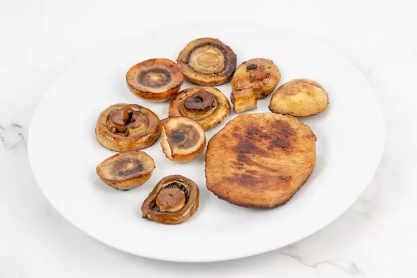 Gebratene Pilze neben einem Stück Schweinekotelett auf einem Teller auf der Küchentheke