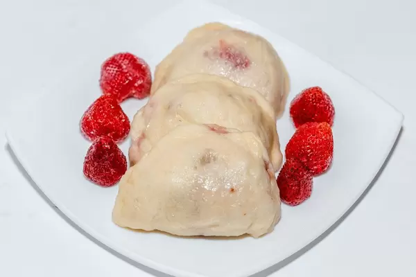 Gedämpfte, gefüllte Knödel angerichtet mit frischen ganzen Erdbeeren auf weißem Teller