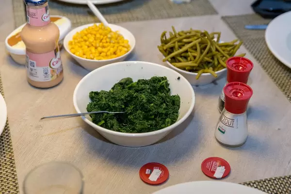 Gedeckter Tisch für Raclette mit Cocktailsoße, Butter, Salz und Pfeffer, Mais, Bohnen und Spinat