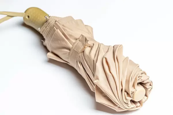 Gefaltener kleiner Regenschirm in beige auf weißem Hintergrund