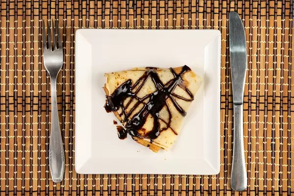 Gefalteter, dreieckiger Pfannkuchen mit Schokolade überzogen auf weißem Teller