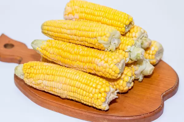 Gefrorene Maiskolben gestapelt auf Holzbrett vor weißem Hintergrund