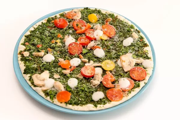 Gefrorene, vegane Fertigpizza Verdura der Trattoria Alfredo, mit Spinat, Cherrytomaten und Champignons vor weißem Hintergrund