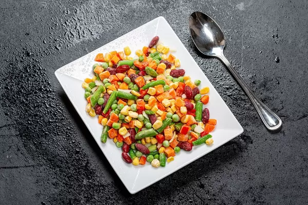 Gefrorenes buntes Gemüse auf einem weißen Teller und schwarzen Hintergrund - Top-view