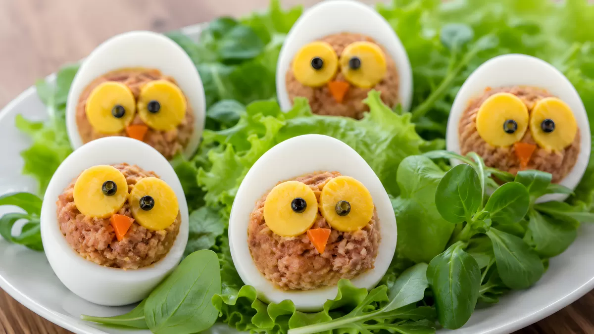 Gefüllte Eier als Eulen dekoriert auf Salatbett