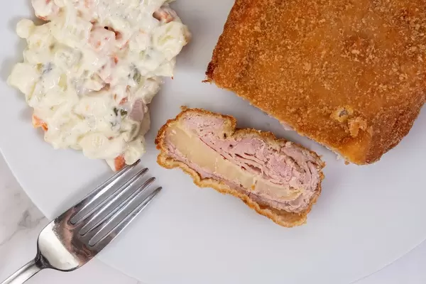 Gefülltes Schweinefleisch mit Käsefüllung und Gemüsesalat, als deftiges Mittagessen, auf einem weißen Teller