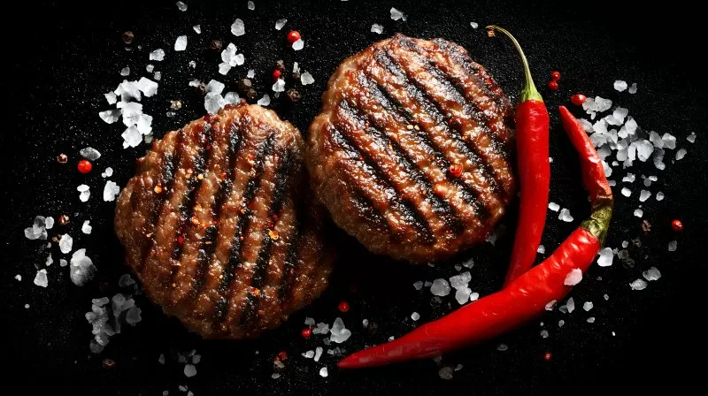 Gegrillte Burgerpatties mit Chili und Salz auf schwarzem Hintergrund