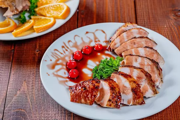 Gegrillte Hähnchenbrust in Scheiben mit Granatapfelsoße auf einem Teller mit gegrillten Kirschtomaten und Petersilie