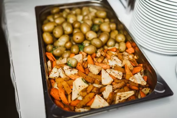 Gegrillte Karotten, Kartoffeln und Sellerie in einem Tablett neben einem Stapel Teller auf einem Tisch