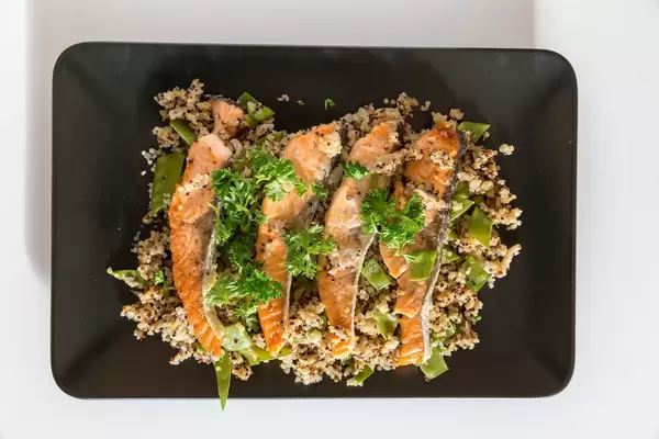 Gegrillte Lachsscheiben auf Blumenkohl-Quinova mit Parmesanchips auf schwarzem Teller