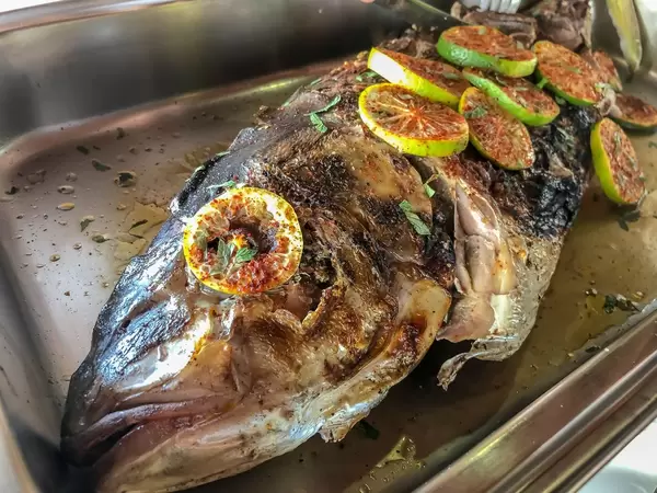 Gegrillter Fisch mit Limonenscheiben dekoriert, in einem Edelstahl-Wärmebehälter