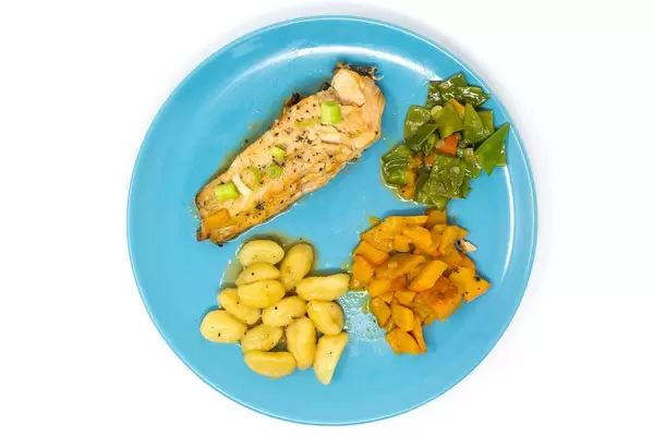 Gegrilltes Lachssteak in Hoisin-Miso Sauce´mit geschwenktem Kürbis-Zuckerschotengemüse und Gnocchi auf hellblauem Teller von oben auf weißem Hintergrund