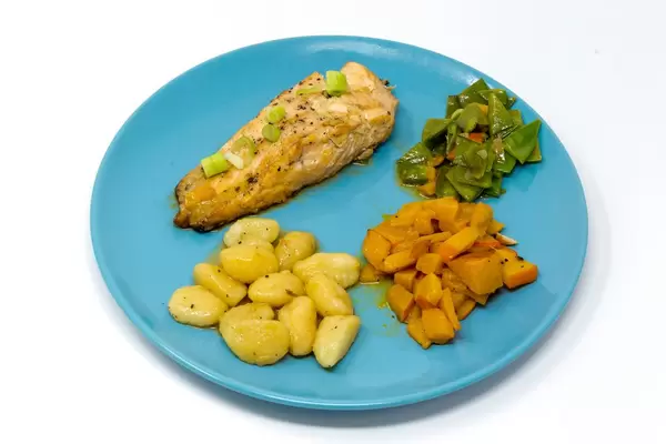 Gegrilltes Lachssteak in Hoisin-Miso Sauce´mit geschwenktem Kürbis-Zuckerschotengemüse und Gnocchi auf hellblauem Teller