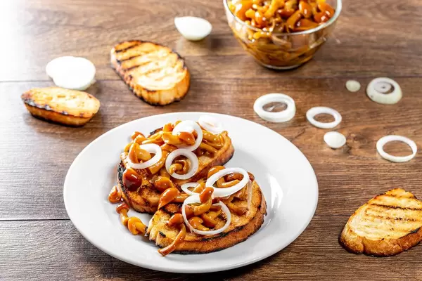 Gegrilltes Sandwichbrot mit Pilzen und Zwiebelringen, auf einem Holztisch