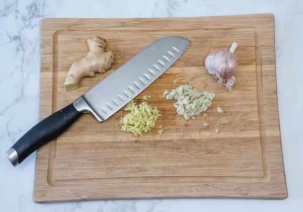 Gehackter Knoblauch und Ingwer mit einem Messer auf Holzschneidebrett