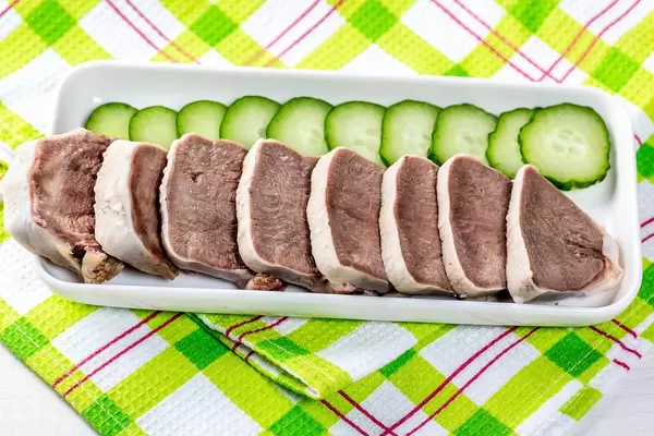 Gekochte und in Scheiben geschnittene Zunge neben Gurkenscheiben, auf einem grünen Abtrockentuch