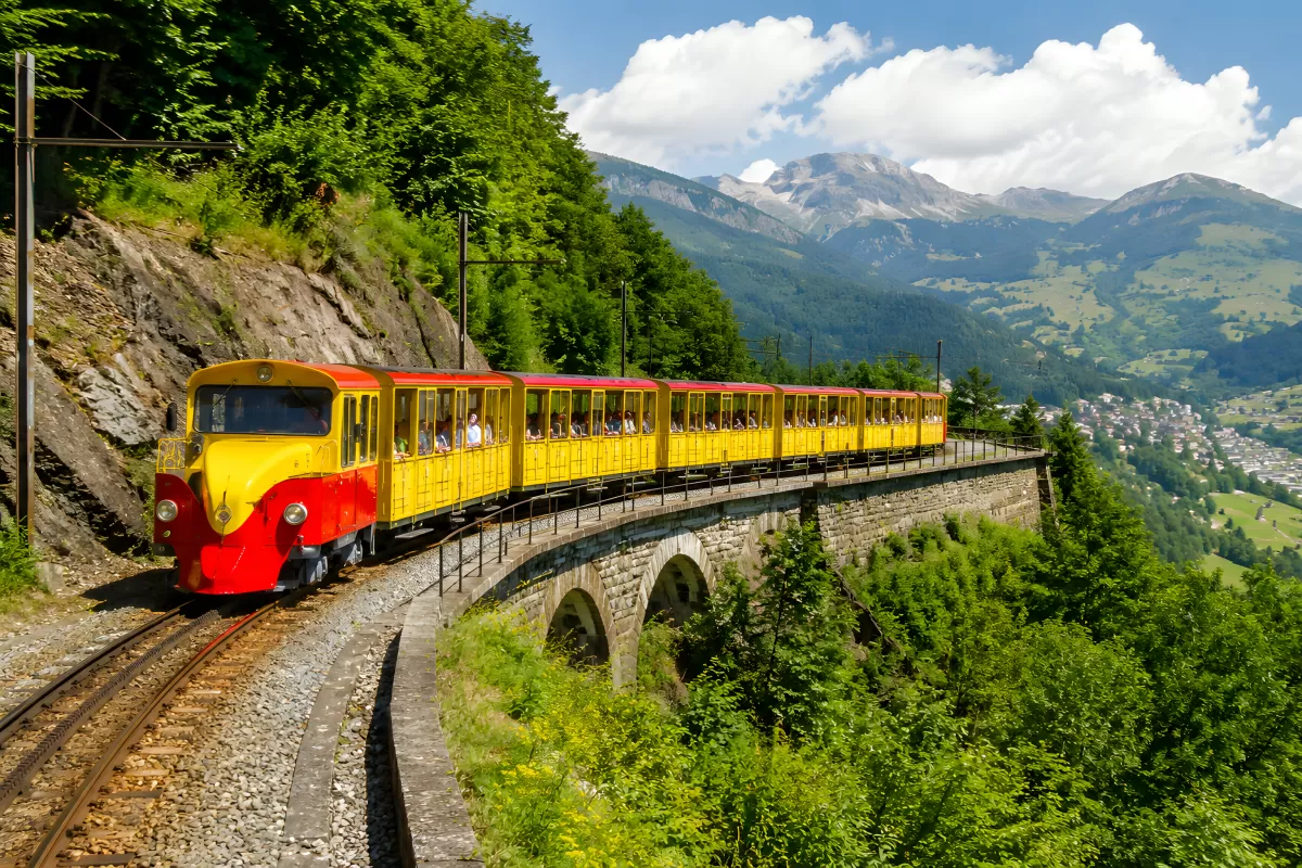 Gelb-roter Bergzug auf Viadukt in den Alpen