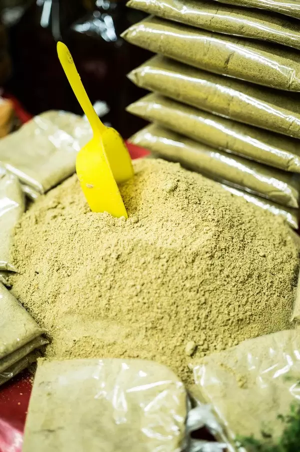 Gelbe Schaufel steckt in grünem Berg von gemahlenen Kürbiskernen, umgeben von in Plastik abgepacktem Kürbiskernmehl