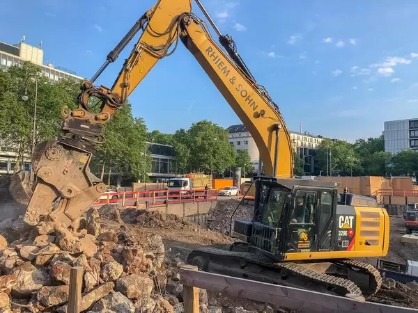 Gelber Bagger arbeitet auf der Baustelle für das Bürohochhaus Wallarkaden am Rudolfplatz, nahe dem Hahnentor in Köln