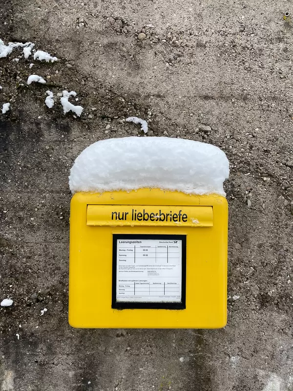 Gelber Briefkasten der Deutschen Post mit einem Aufkleber "Nur Liebesbriefe" und einer Schneedecke darauf