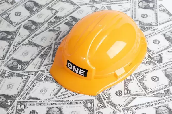 Gelber Schutzhelm für Bauarbeiter auf verteilten Banknoten symbolisiert Bauindustrie