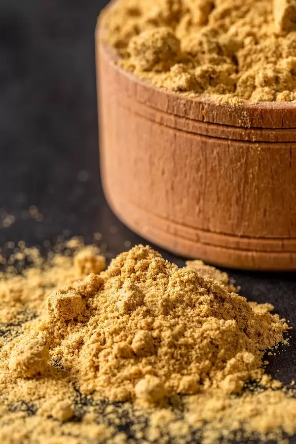 Gemahlene Senfkörner in Holzschüssel und auf schwarzem Tisch