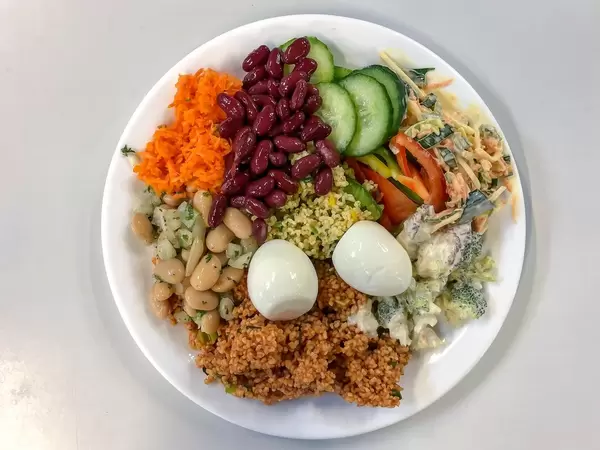 Gemischter Salat mit gekochtem Ei, Bohnen, Gurken, Karotten, Brokkoli und Couscous auf weißem Teller