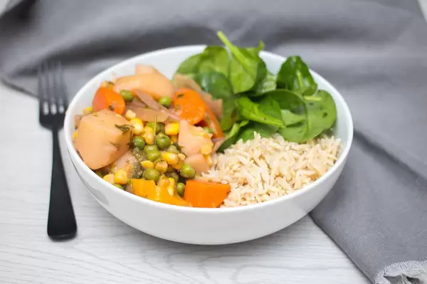 Gemüse-Curry aus Karotten, Kartoffeln, Erbsen uns Mais mit Reis und Baby-Spinat in einer Schüssel