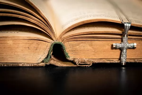 Geöffnete, alte Bibel mit verfärbten Seiten und kunstvollem, silbernem Kreuz als Buchzeichen