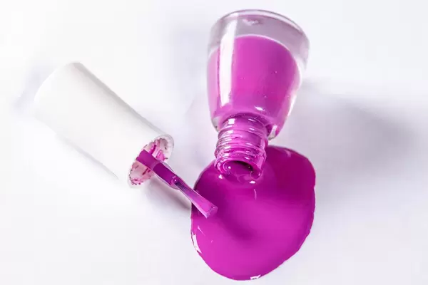 Geöffnete Flasche mit violettem Nagellack wurde auf weißem Tisch verschüttet