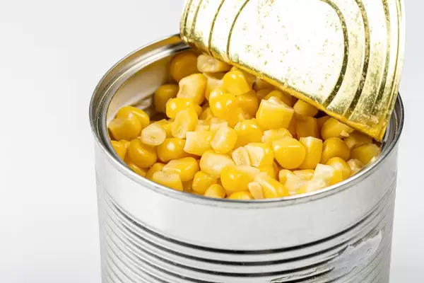 Geöffnete Konservendose mit Maiskörnern vor weißem Hintergrund