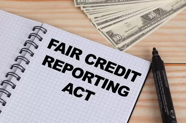Geöffnetes Notebook mit schwarzem Text Fair Credit Reporting Act mit schwarzem Filzstift und Dollar Geldscheinen auf einem Holztisch