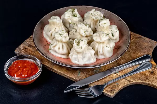 Georgian khinkali with sauce on a black plate with knife and fork