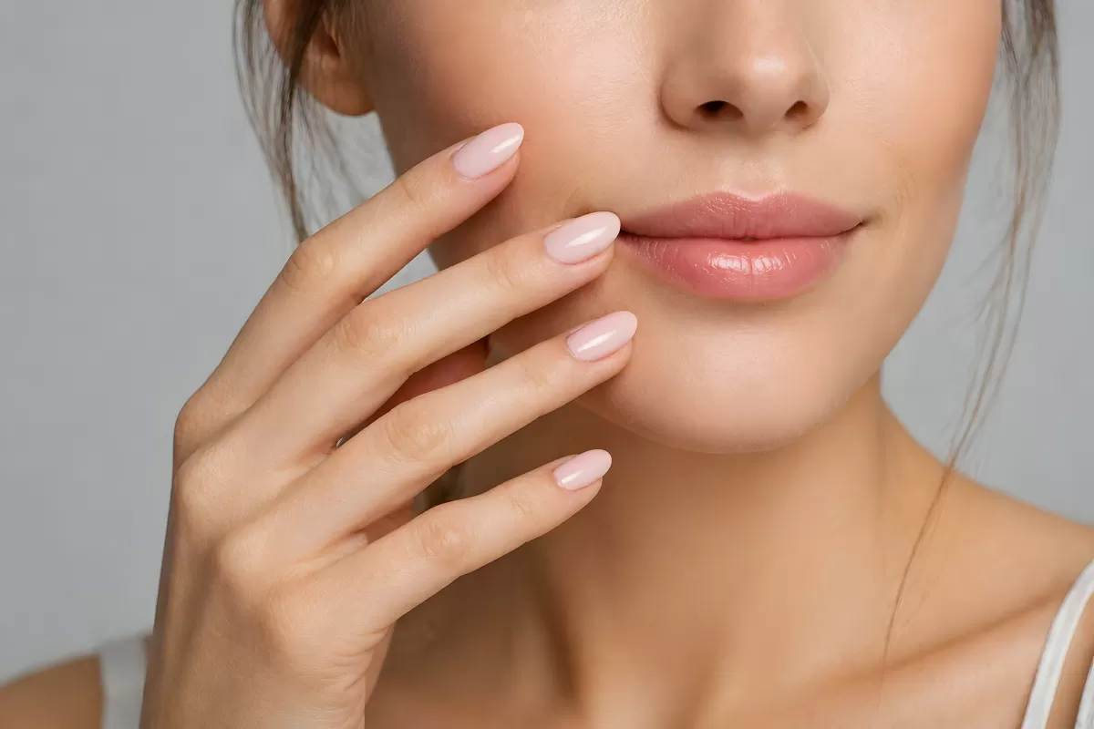 Gepflegte Hände mit rosa Nägeln neben weichen Lippen