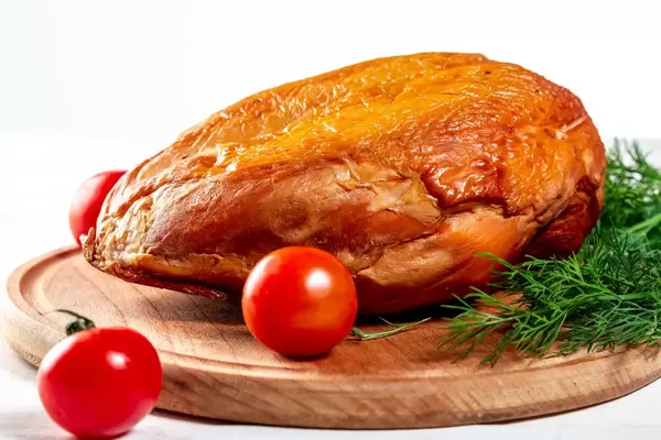 Geräucherte Hühnerbrust auf einem runden Holzbrett mit Dill- und Kirschtomaten