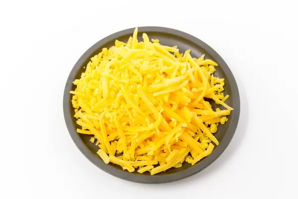 Geriebener Cheddar auf einem schwarzen Teller auf weißem Hintergrund