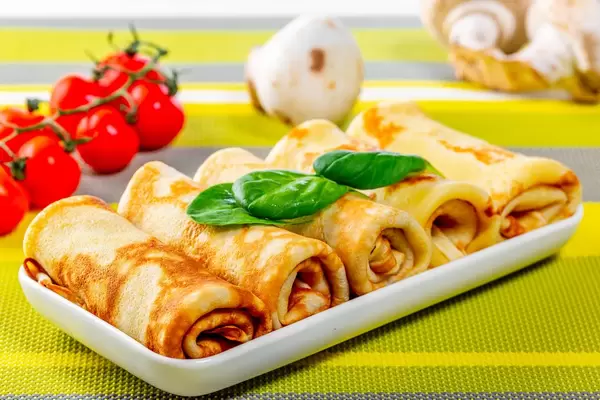 Gerollte Pfannkuchen mit Pilzen, Tomaten und frischem Basilikum auf einem Tisch