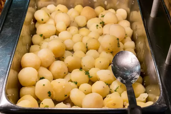 Geschälte, ganze Kartoffeln in einem Wärmebehälter aus Edelstahl mit einem Löffel, am Mittagsbüfett
