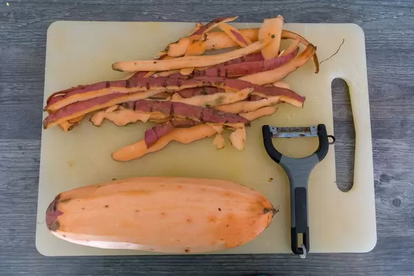 Geschälte Süßkartoffel mit Schäler und Schale auf Schneidebrett