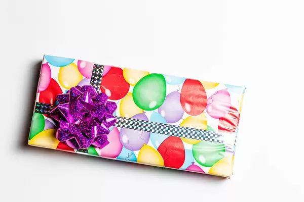 Geschenk in Geburtstags-Geschenkpapier verziert mit einer lila Stern Schleife auf weißem Hintergrund Draufsicht