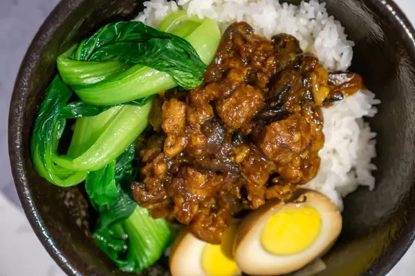 Geschmortes Schweinefleisch, Entenei, Bok Choy Gemüse und Reis als Taiwainesische Reis-Bowl in einer schwarzen Keramikschale Nahaufnahme