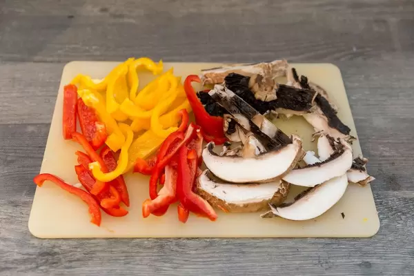 Geschnittene frische Pilze mit roten und gelben Paprikastreifen auf einem Schneidebrett