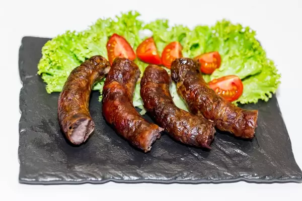 Geschnittene, gebratene Wurst auf schwarzer Schieferplatte, dekoriert mit grünem Salat und Tomaten
