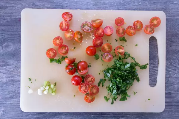 Geschnittene Kirschtomaten mit gehackter Petersilie und Frühlingszwiebeln auf Plastikbrett